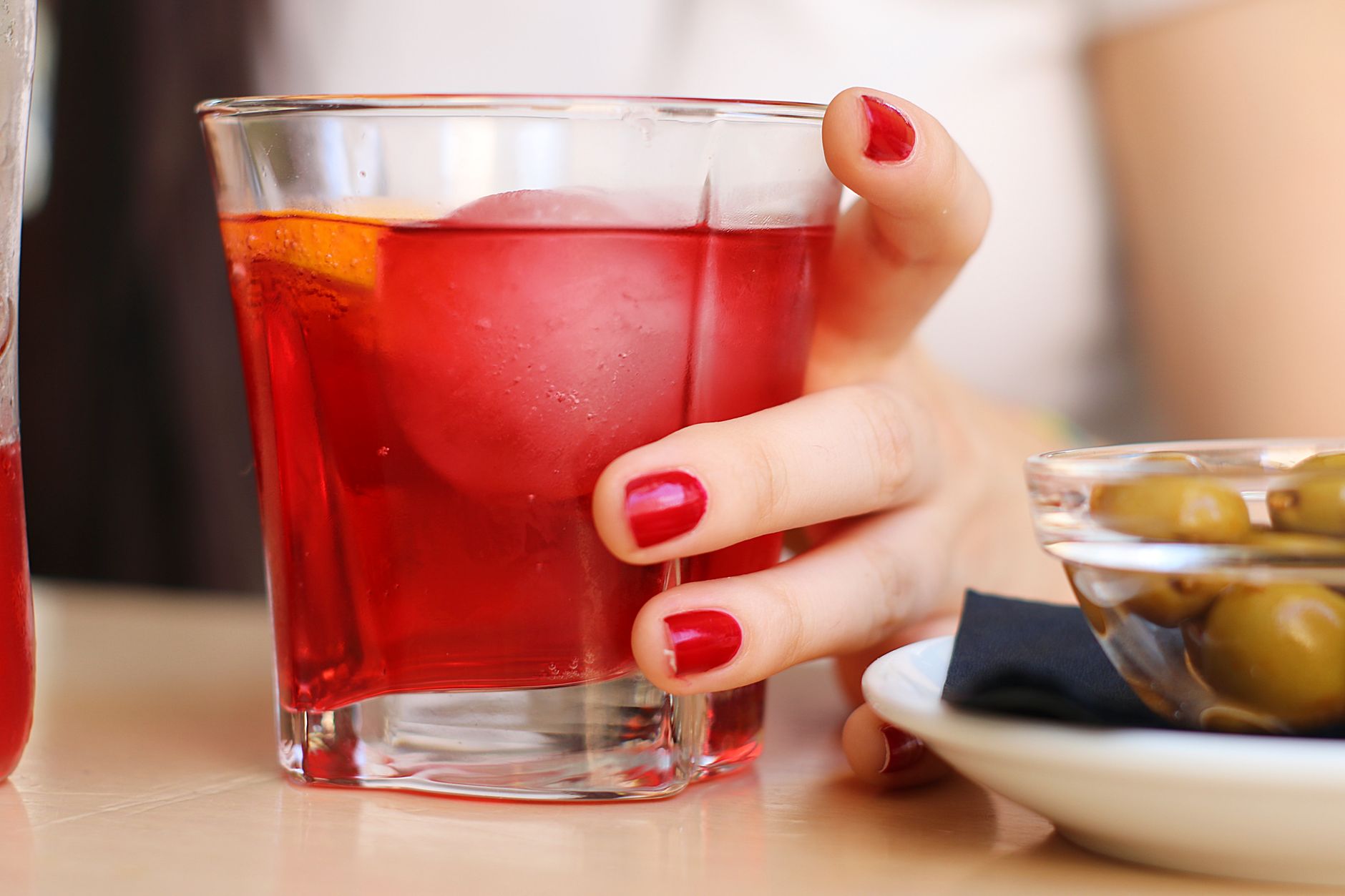 Verschillende flessen gin naast een geroerde Negroni cocktail met sinaasappelschil op een bartafel